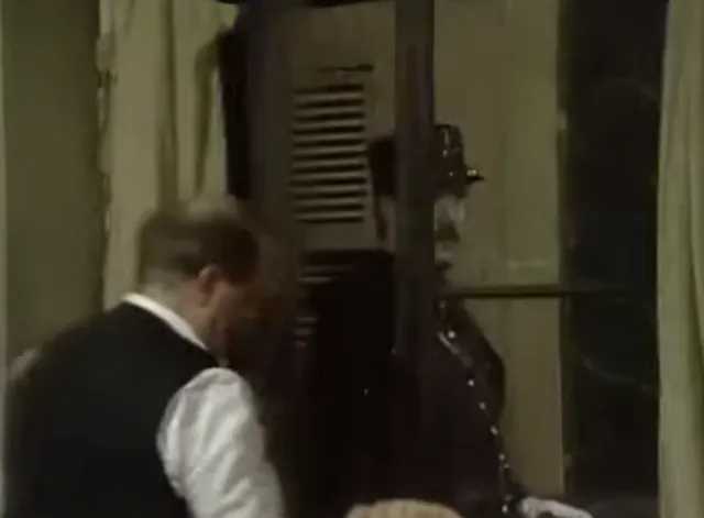 A man in a vest and jacket appears to be struggling or pushing against a large dark door or shutter in what looks like a period drama or film scene. The image is grainy and low resolution, suggesting it is a screenshot from an older television production or movie.