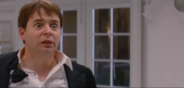 A man in a dark blazer and open-collar shirt stares wide-eyed with a shocked, open-mouthed expression, standing in front of French doors. The scene appears to be from the movie Ferris Bueller's Day Off, capturing a moment of surprise or disbelief.