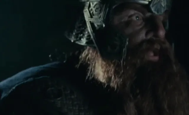A close-up shot of Gimli the dwarf from Lord of the Rings, wearing his ornate dwarven helmet and chainmail, with a thick red beard, looking upward with a determined or awestruck expression in a dark setting.