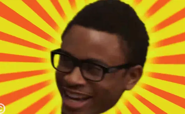 A young Black man wearing thick-framed glasses grins broadly against a bold yellow and orange sunburst pattern background. The image has a reaction meme format suggesting excitement, approval, or pleasant surprise.